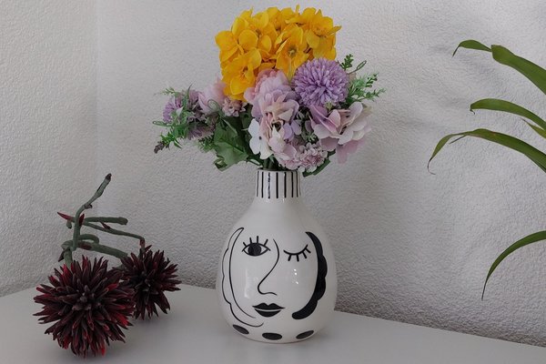 moderne Vase in schwarz und weiss mit Gesicht, geschmückt von einem schönen buten blumen strauß